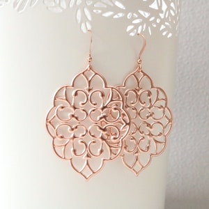 Puede incluir: Pendientes de filigrana de oro rosa con un dise&ntilde;o delicado e intrincado. Los pendientes tienen forma de flor con un centro circular y m&uacute;ltiples capas de p&eacute;talos.