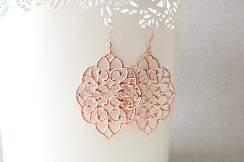 Puede incluir: Pendientes de filigrana de oro rosa con un dise&ntilde;o delicado e intrincado. Los pendientes tienen forma de flor con un centro circular y m&uacute;ltiples capas de p&eacute;talos.