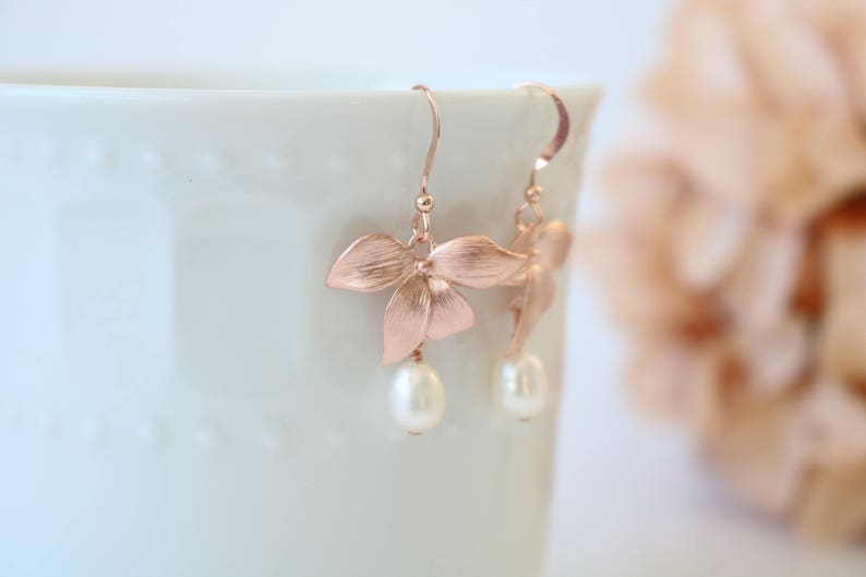 May include: Rose gold earrings with a delicate flower design and a pearl drop.