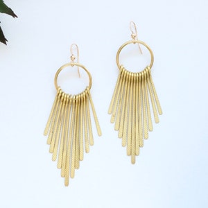 May include: Gold hoop earrings with a fringe of thin, textured metal bars hanging from the bottom.