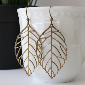 Peut inclure: Une paire de boucles d'oreilles en forme de feuille dorée avec un design délicat et complexe. Les boucles d'oreilles sont en métal et ont un style pendentif.
