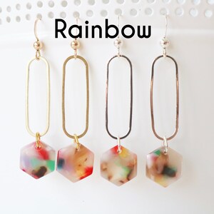 May include: Four pairs of dangle earrings with a hexagonal charm. The charms are made of clear resin with colourful flecks. The earrings are available in gold, silver, and rose gold.
