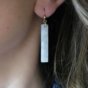 Peut inclure: Boucles d'oreilles pendantes rectangulaires blanches avec un crochet doré et un motif marbré blanc.