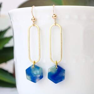 May include: Gold dangle earrings with a blue and white marbled hexagon pendant.