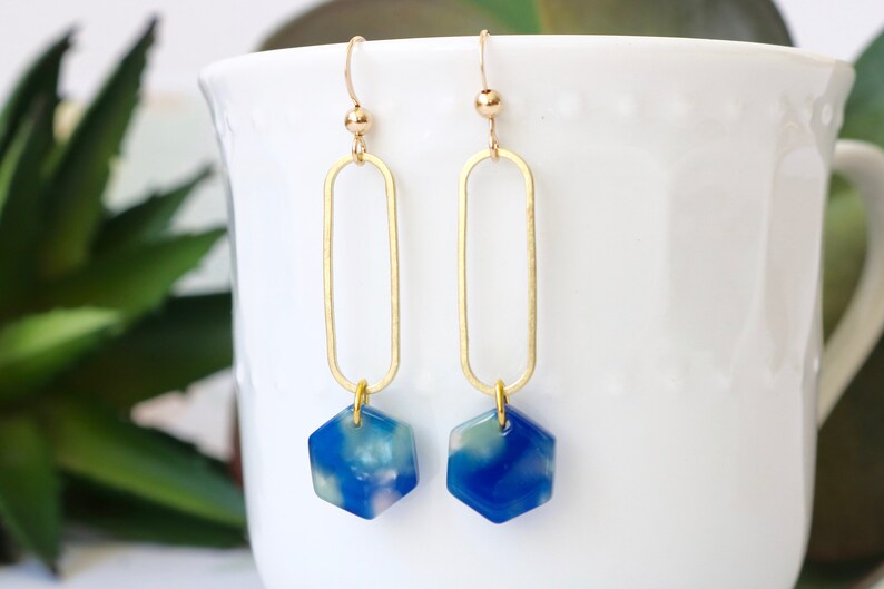 May include: Gold dangle earrings with a blue and white marbled hexagon pendant.