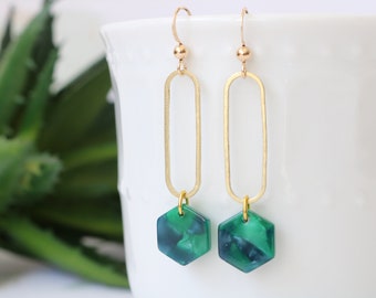 May include: Gold dangle earrings with a green hexagon-shaped pendant. The pendant has a marbled pattern.