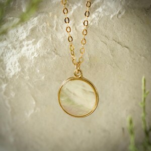 May include: A gold chain necklace with a round, white mother-of-pearl pendant.