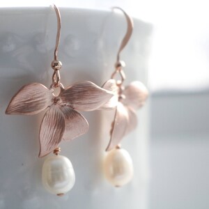 May include: Rose gold flower earrings with a pearl drop. The earrings are delicate and feminine.