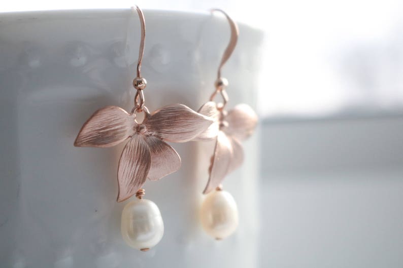 May include: Rose gold flower earrings with a pearl drop. The earrings are delicate and feminine.
