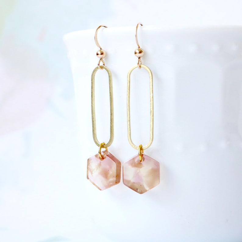 May include: Gold dangle earrings with a pink and white hexagonal shaped pendant.