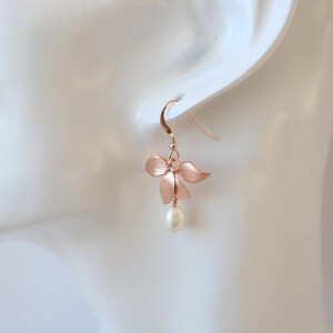 May include: Rose gold flower earrings with a single pearl drop. The flower is made of metal and has a delicate, feminine design.