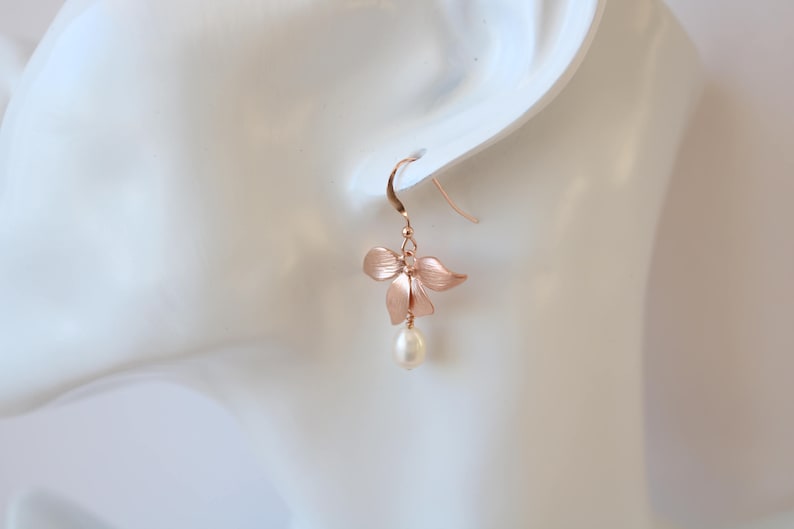 May include: Rose gold flower earrings with a single pearl drop. The flower is made of metal and has a delicate, feminine design.