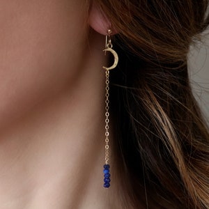May include: Gold crescent moon earrings with a delicate chain and blue gemstone accents.