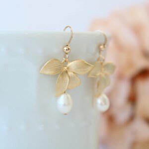 May include: Gold orchid flower earrings with a pearl drop. The earrings are delicate and feminine.