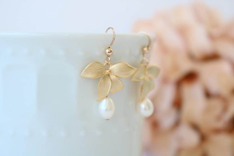 May include: Gold orchid flower earrings with a pearl drop. The earrings are delicate and feminine.
