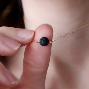 May include: A delicate gold chain necklace with a single black lava rock bead.
