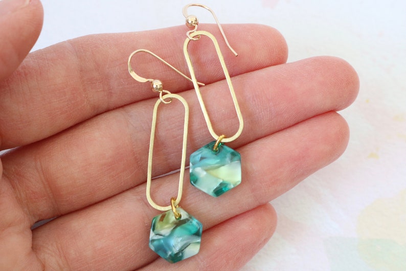 May include: Gold earrings with a teardrop-shaped design and a hexagonal green and white stone pendant.