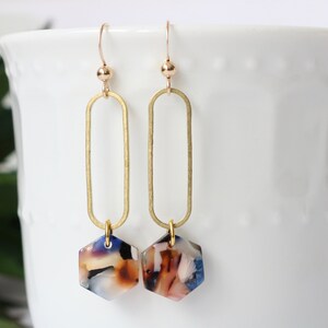 May include: Gold oval hoop earrings with a hexagonal, multi-coloured, marbled resin pendant.