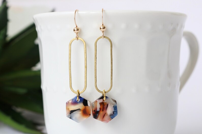 May include: Gold oval hoop earrings with a hexagonal, multi-coloured, marbled resin pendant.