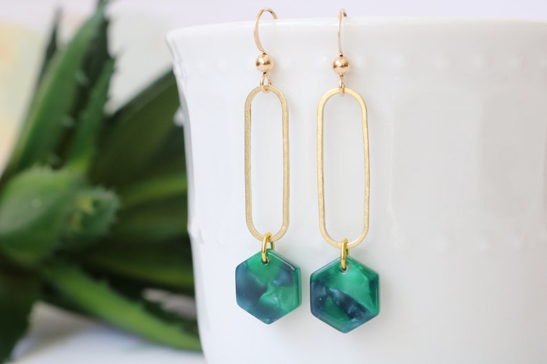 May include: Gold dangle earrings with a green hexagon-shaped pendant. The pendant has a marbled pattern.