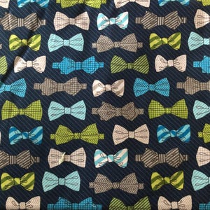 May include: A navy blue fabric with a repeating pattern of colorful bow ties. The bow ties are in various colors and patterns, including green, blue, white, and gray.