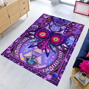 Puede incluir: Una alfombra rectangular con un diseño vibrante en tonos morados y rosas al estilo de vidrieras. El gráfico central muestra una máscara grande y estilizada con ojos amarillos brillantes, rodeada de patrones geométricos, símbolos y el texto Final.