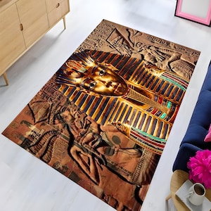 May include: A gold and brown rug with an intricate design featuring a pharaoh's face and hieroglyphics.