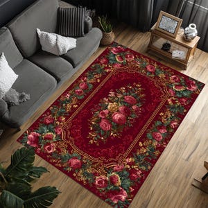 Puede incluir: Una alfombra rectangular roja con un diseño floral. La alfombra presenta un ramo central de rosas rosas y amarillas, rodeado por un borde dorado y un marco de rosas y hojas verdes. Está colocada sobre un suelo de madera.