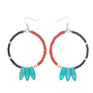 May include: A pair of hoop earrings with a beaded design. The hoops are divided into sections of black, red, and white beads. Each earring has three turquoise teardrop-shaped charms hanging from the bottom.