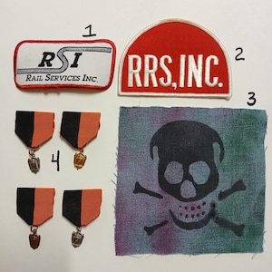 May include: Four patches, two black and orange, two red and white, with the text "RSI Rail Services Inc." and "RRS, INC."  Two black and orange medals with gold and silver accents. A blue and purple fabric patch with a black skull and crossbones.
