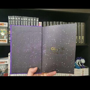 Pode incluir: Um livro de capa dura com uma capa de cor roxo escuro e um design de c&eacute;u estrelado. O t&iacute;tulo "Glory To The 41" est&aacute; impresso em dourado na capa.