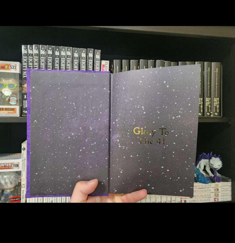 Pode incluir: Um livro de capa dura com uma capa de cor roxo escuro e um design de c&eacute;u estrelado. O t&iacute;tulo "Glory To The 41" est&aacute; impresso em dourado na capa.