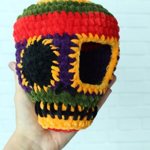 May include: A colorful crocheted skull with a black eye socket, made with green, red, yellow, purple, and black yarn.