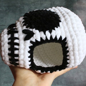 Può includere: Teschio in crochet bianco con dettagli in velluto nero. Il teschio ha una grande benda nera sull'occhio e una bocca in crochet nero.