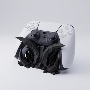 Könnte beinhalten: Ein weiß-schwarzer kabelloser Videospiel-Controller, der auf einem schwarzen, zerklüfteten, felsartigen Ständer ruht. Der Controller verfügt über ein zentrales PlayStation-Logo, zwei Analogsticks, ein Steuerkreuz und vier Aktionstasten.