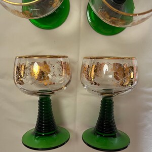 Puede incluir: Copas de vino transparentes con bordes dorados y dise&ntilde;os de uvas. Los tallos son de color verde oscuro con un dise&ntilde;o acanalado y las bases son de color verde liso. Las copas son probablemente vintage y a&ntilde;aden un toque de elegancia.