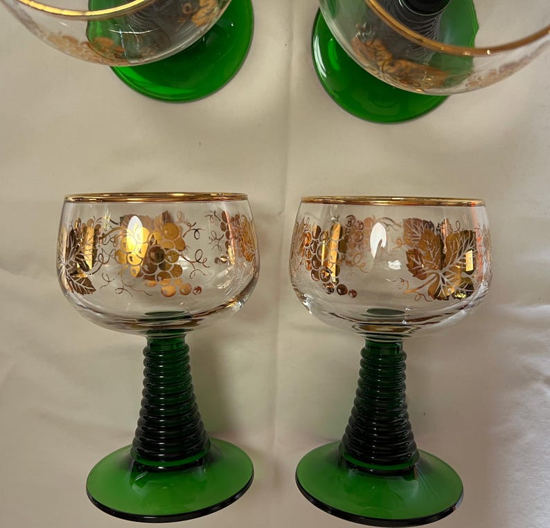 Puede incluir: Copas de vino transparentes con bordes dorados y dise&ntilde;os de uvas. Los tallos son de color verde oscuro con un dise&ntilde;o acanalado y las bases son de color verde liso. Las copas son probablemente vintage y a&ntilde;aden un toque de elegancia.