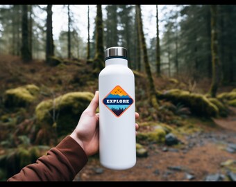 Könnte beinhalten: Weiße Wasserflasche mit einem rautenförmigen Aufkleber, der eine Berglandschaft, einen Sonnenuntergang und das Wort "EXPLORE" in blauer Schrift zeigt.