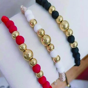 May include: Three beaded bracelets with gold beads and different colored cords. The bracelets are red, white, and black.