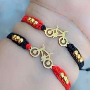 May include: Two bracelets with black and red string and gold beads. Each bracelet has a gold charm in the shape of a motorcycle.
