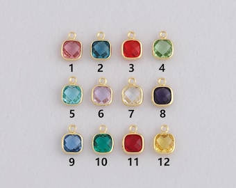 May include: A collection of twelve square-cut gemstone charms in various colors, including pink, blue, red, and green. Each charm has a gold-colored loop at the top for attaching to a necklace or bracelet. The charms are arranged in three rows of four.