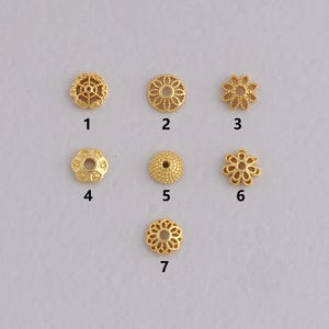 May include: Seven gold-colored metal bead caps in various floral and geometric designs. The caps are small, with intricate patterns, and are displayed against a light background. These decorative components are suitable for jewelry making and crafting projects.