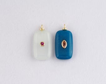 Puede incluir: Dos colgantes rectangulares con esquinas redondeadas. Uno es blanco con una gema roja, el otro es verde azulado con una gema roja. Ambos tienen lazos dorados en la parte superior para colgar.