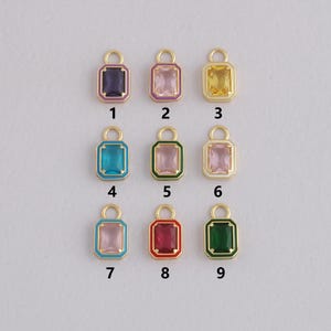 May include: Nine colorful rectangular charms with gold-colored borders and loops. The charms feature various colors, including purple, pink, yellow, teal, light pink, red, and green. Each charm has a rectangular gemstone shape.