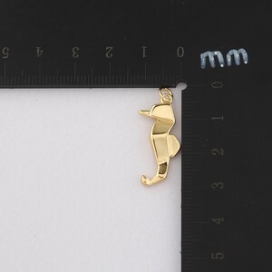 K&ouml;nnte beinhalten: Goldfarbener Seepferdchen-Anh&auml;nger. Das Seepferdchen ist mit geometrischen Formen stilisiert und hat oben eine kleine Schlaufe f&uuml;r eine Kette. Der Anh&auml;nger ist etwa 2,5 cm lang.