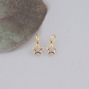 Peut inclure: Deux breloques en forme d'étoile dorées avec une boucle en haut. Les étoiles sont creuses et ont une finition lisse et polie.