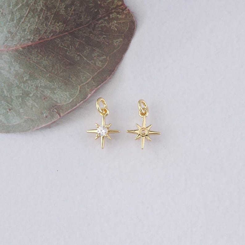 Op de afbeelding: Twee goudkleurige sterbedels met een heldere strasssteen in het midden. De bedels hebben een lus aan de bovenkant om aan sieraden te bevestigen.