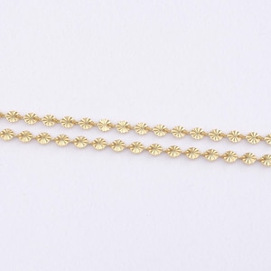 May include: Two strands of delicate gold-colored chain. Each chain is composed of small, evenly spaced, circular elements with a starburst pattern. The chains are set against a plain white background.