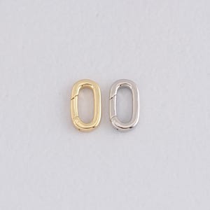 May include: Two oval-shaped jewelry clasps. One clasp is gold-colored, and the other is silver-colored. Both clasps have a hinged design for easy opening and closing. The clasps are set against a plain white background.
