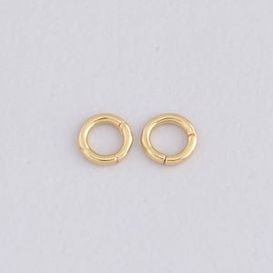 May include: Two gold-colored, circular jewelry clasps. Each clasp is a complete circle with a small opening for attachment. The clasps are made of a shiny, metallic material and are set against a white background.